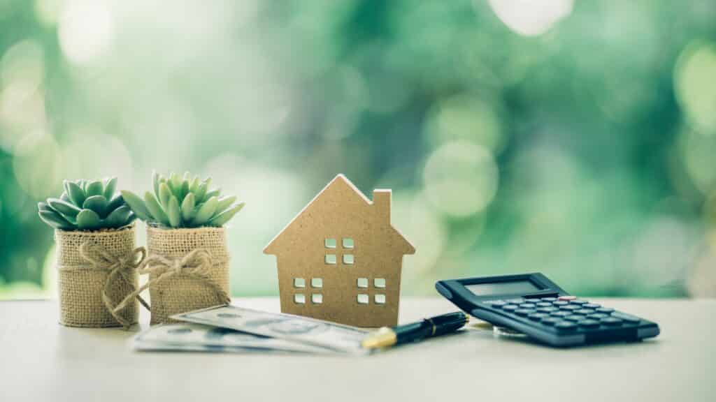 Property investment concept. Wooden house, dollar bill and calculator on table. Pen prepare planning savings money to buy a home, mortgage and real estate investment.
